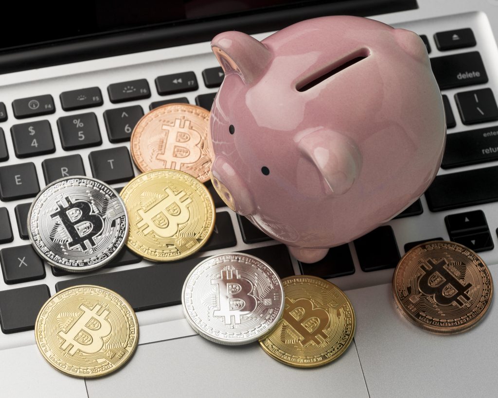 An image of a piggy bank and some crypto currencies on a keyboard part of a laptop