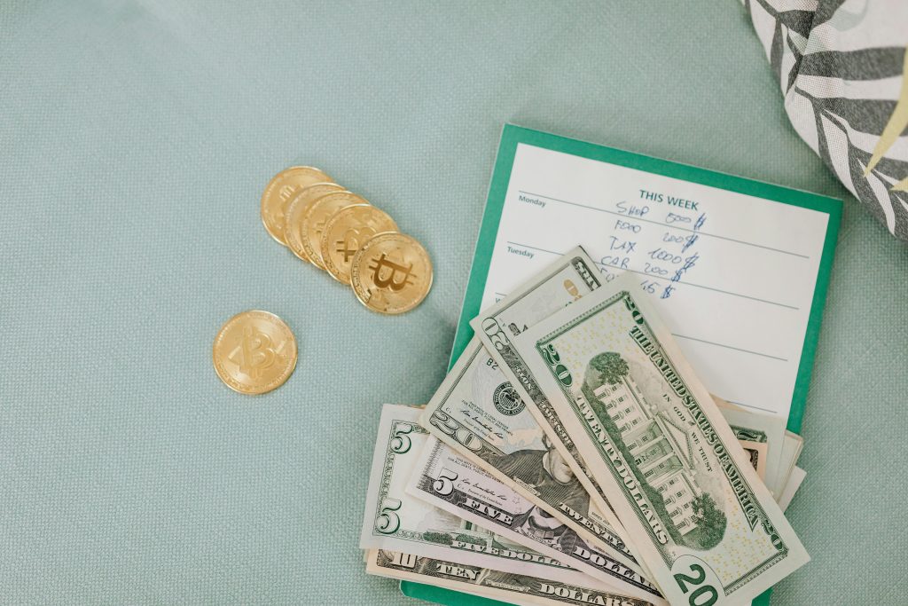 An image of a notepad with crypto coins beside it and a stack of dollar bills arranged on a table symbolizing financial planning and investment strategies