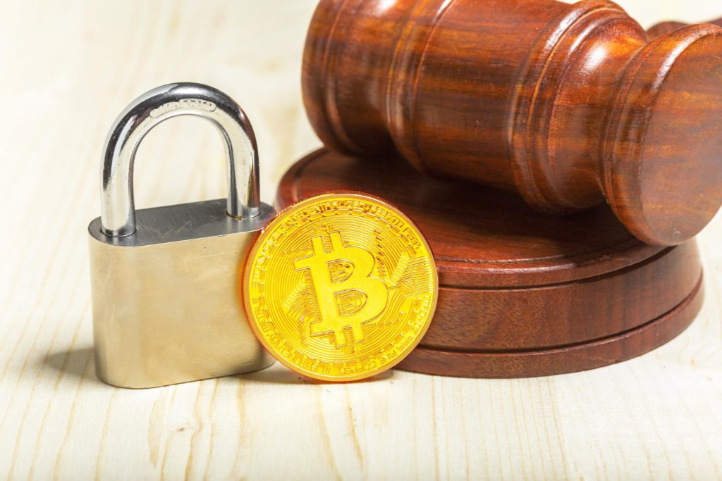 An image depicting bitcoin coin next to a padlock and a judge's gavel, symbolizing cryptocurrency regulation, security and legal policies