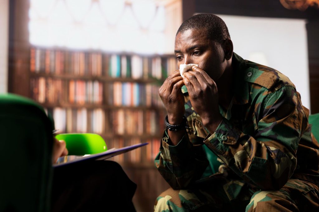 An Image of a black man dressed in an army outfit, sitting in front of a Therapist to share his story