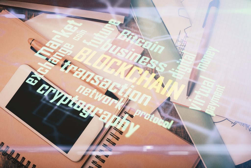 Double exposure image of a smartphone on a table with blockchain-themed holographic graphics, representing cryptocurrency and digital finance technology.