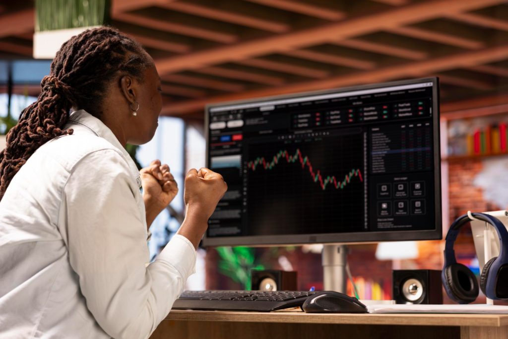 A woman celebrating in front of a computer screen displaying cryptocurrency market charts