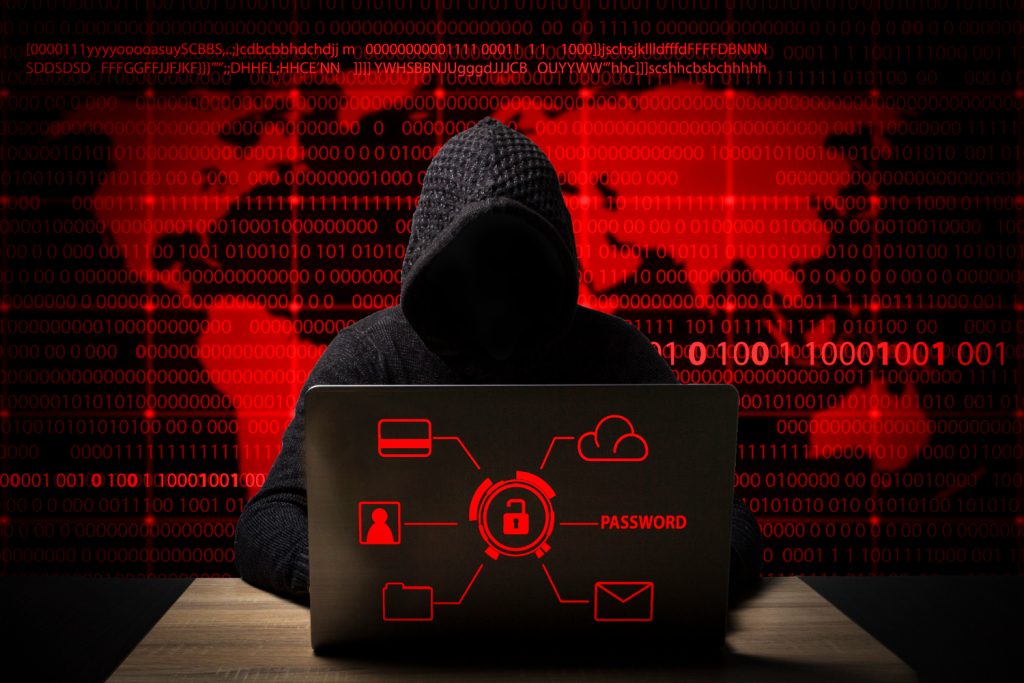 Hacker in a dark hoodie using a laptop with red security icons and binary code in the background, symbolizing a cyberattack or data breach.