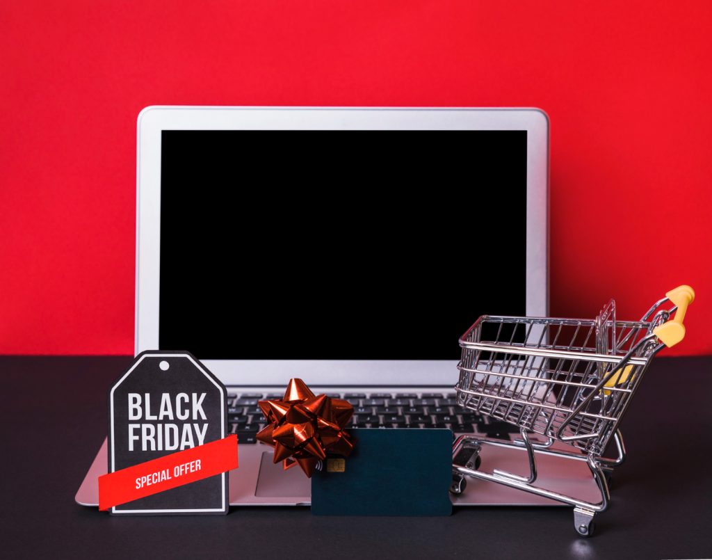 A laptop with a shopping cart and a Black Friday sticker wrapped with a ribbon, representing online Black Friday deals and holiday discounts.
